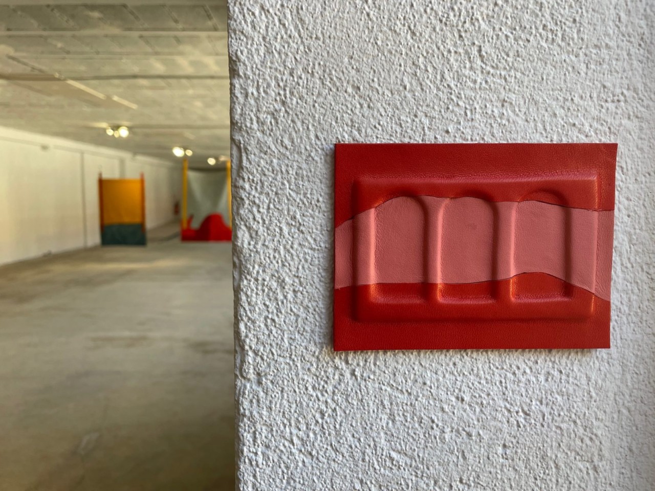 Petit bas-relief rouge et rose accroché à un mur avec salle en fond