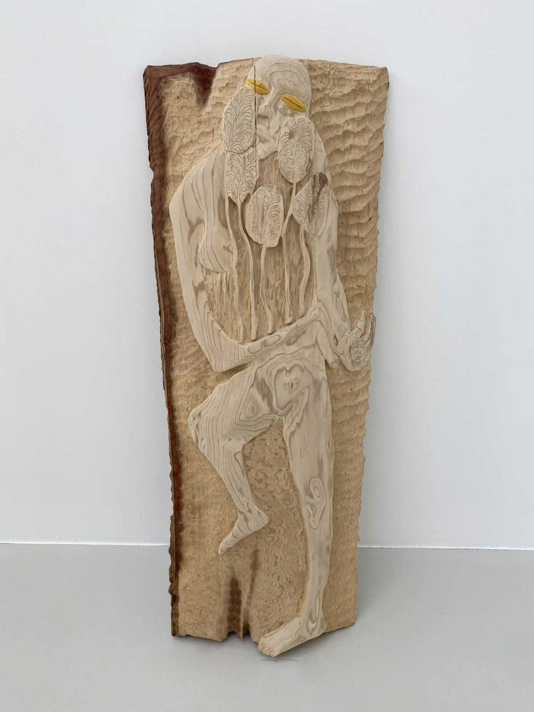 On voit un bois de séquoia de 150 centimètres de haut pour 60 centimètres de large. Dans le bois est scuplté une figure humaine tenant des fleurs entre ses bras.