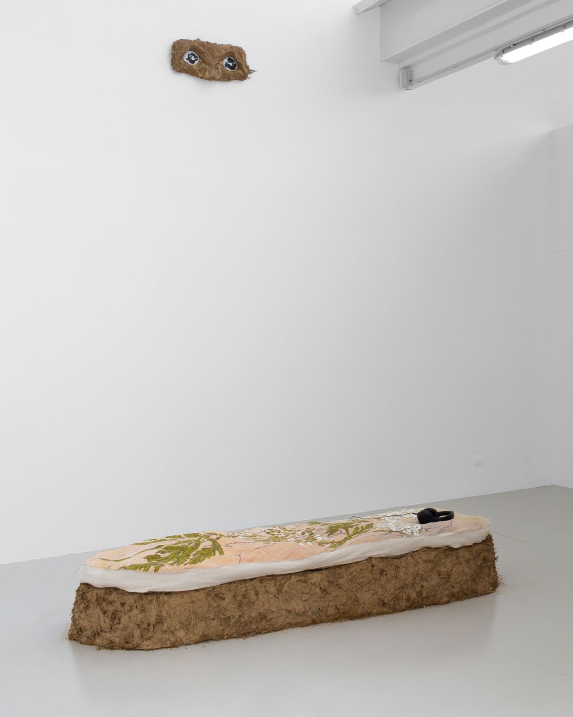 Banc de terre et de tissu rembouré par du foin en dessous de deux yeux en céramiques et en foin.