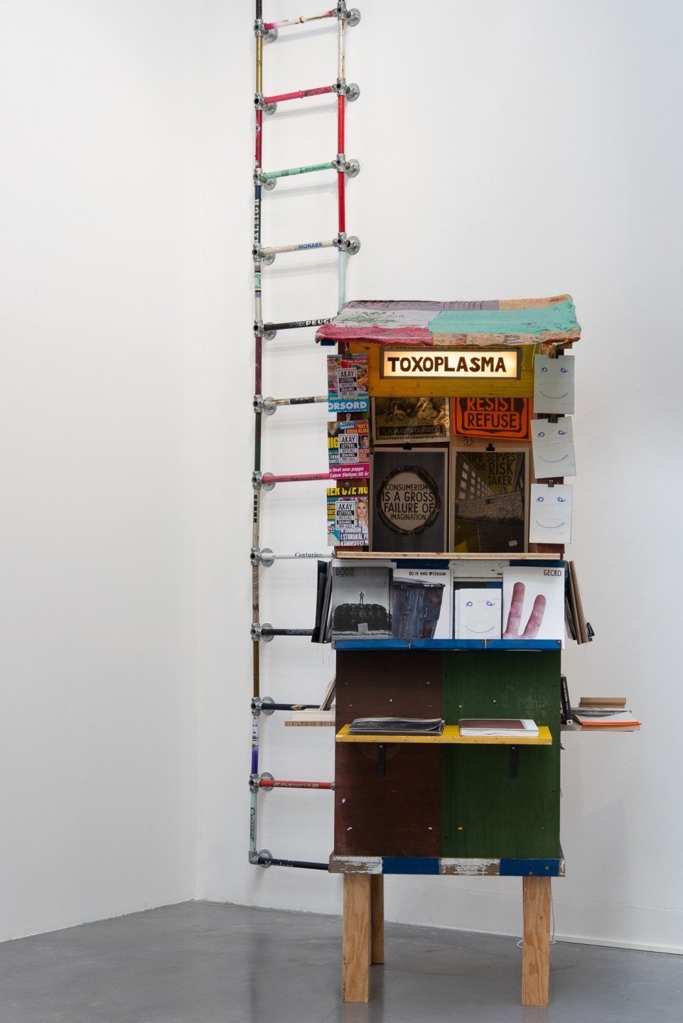 Une échelle en cadre de vélo est suspendue au mur. Devant se trouve un kiosque.