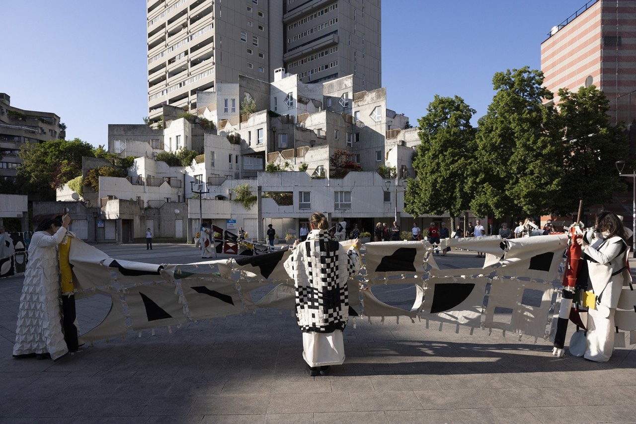 Activation par 10 performeurs des costumes et bannières présentés dans l'exposition de l'artiste, lors d'une procession au sein de l'architecture ivryenne les ayant inspirés