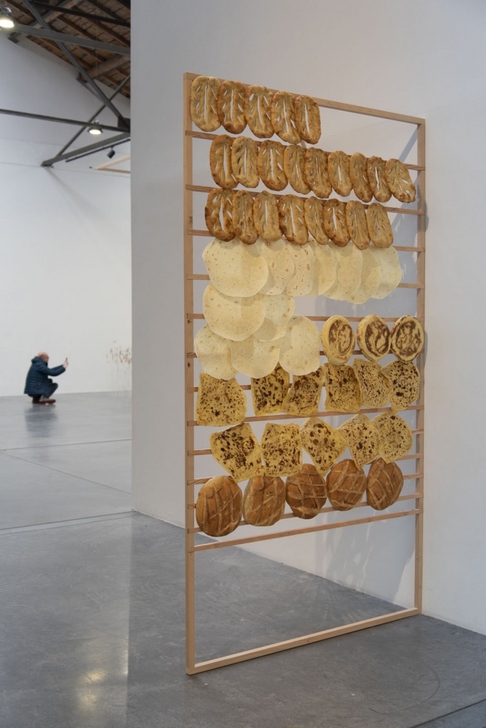 Une structure en bois porte une série de pains plats de différentes orgines que l'artiste a souhaité rassembler afin de constituer une bibliothèque de pains.