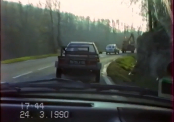 Vue à travers un parebrise de vouture sur le derrière d'une autre voiture. La date et l'heure sont inscrits sur l'image : 17:44 le 24.03.1990