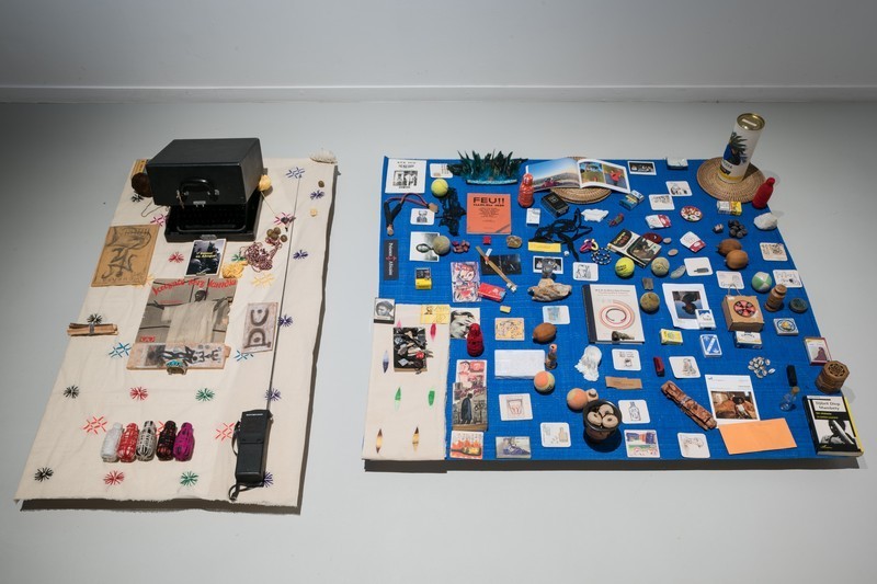 Installation de deux collections d'objets divers minutieusement installé sur des tissus, l'un de couleur beige et de forme rectangulaire et l'autre de couleur bleue et de forme carré