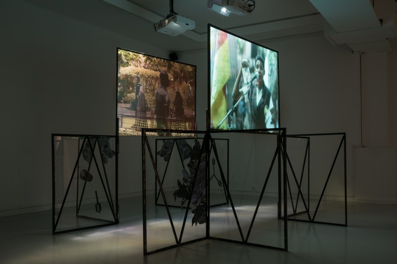 L'oeuvre est une installation au sol, plongée dans l'obscurité, avec deux projections vidéo sur écrans fixés à une structure métallique géométrique de plusieurs carrés, ornés de fleurs séchées