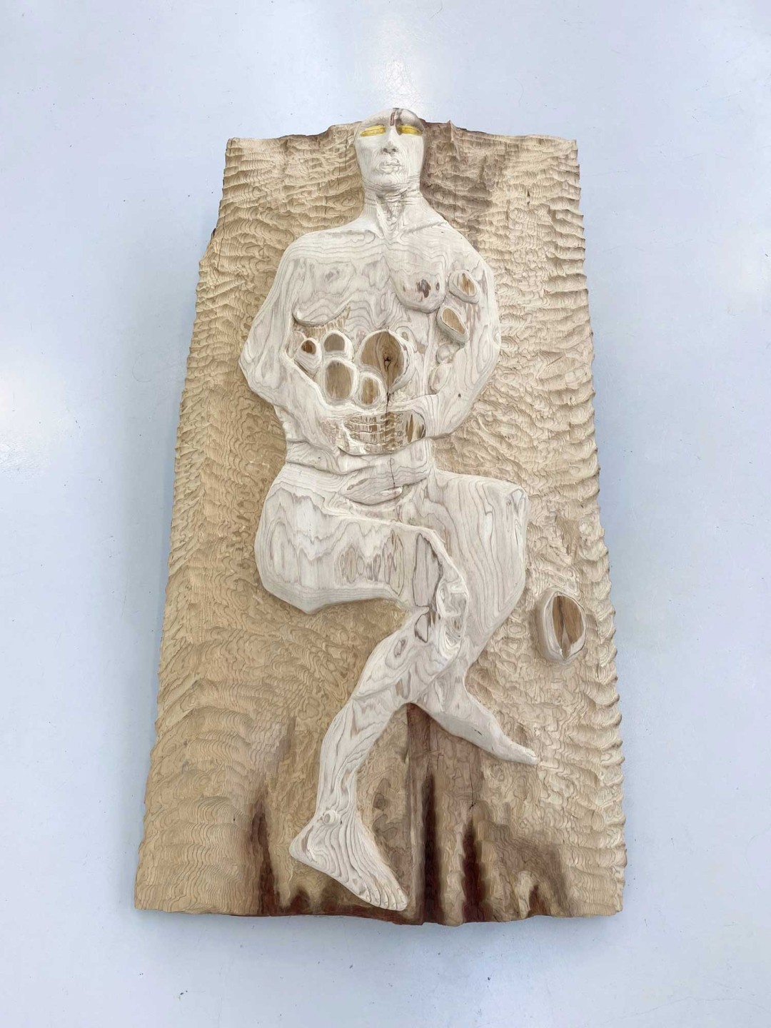On voit un bois de séquoia de 145 centimètres de haut sur 85 centimètres de large. Dans le bois est sculpté une figure humaine portant des fruits.