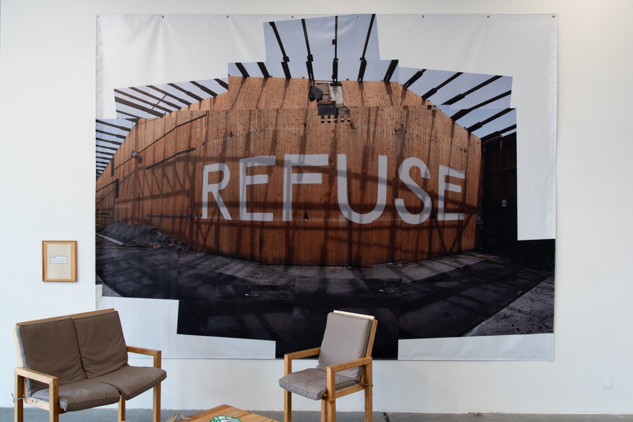 Une photo imprimée sur bâche montre une palissade sur laquelle il est écrit REFUSE